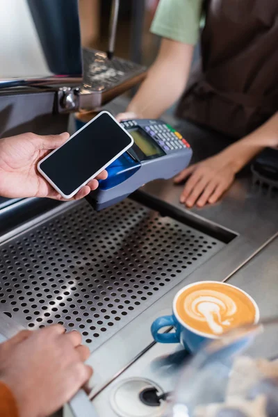 Ausgeschnittene Ansicht eines afrikanisch-amerikanischen Kunden, der in der Nähe von Barista und Kaffee im Café mit dem Handy bezahlt — Stockfoto