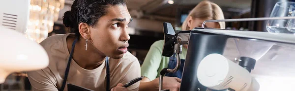 Afroamerikanischer Barista schreibt auf Notizbuch neben Kaffeemaschine und Kollege im Café, Banner — Stockfoto