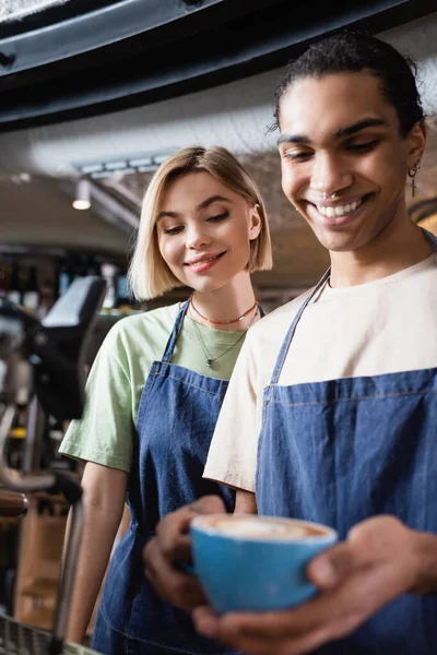 Baristas multiétnicos positivos mirando la taza de café en la cafetería - foto de stock