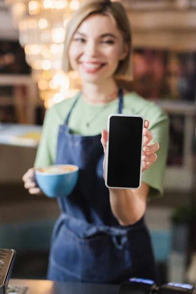 Cellulare con schermo bianco in mano di barista con tazza in caffè — Foto stock