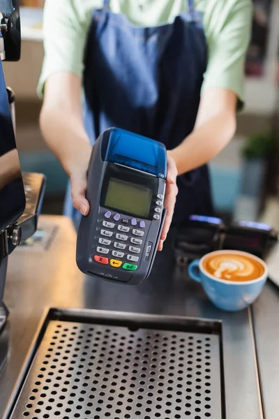 Ausgeschnittene Ansicht eines verschwommenen Barista mit Zahlungsterminal in der Nähe von Kaffee im Café — Stockfoto