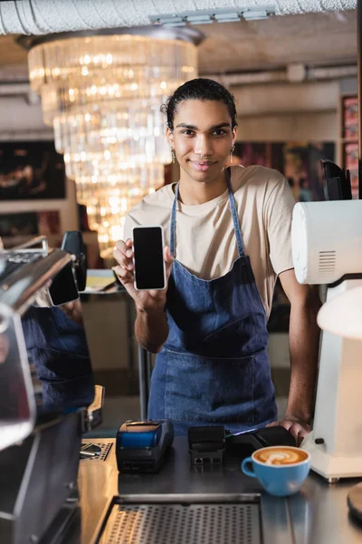 Молодий афроамериканський бариста, що показує смартфон з порожнім екраном біля кави в кафе — стокове фото