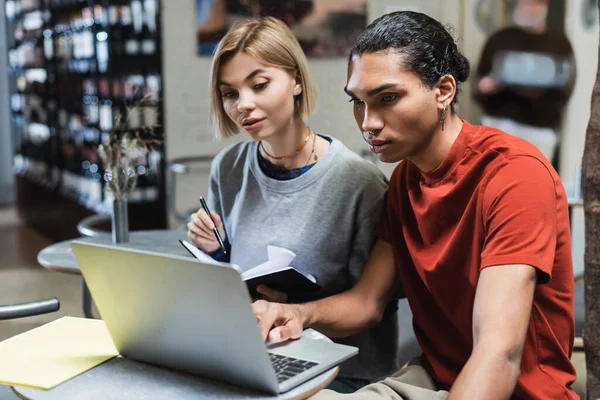 Interracial freelancers with laptop and notebook in cafe — Stock Photo