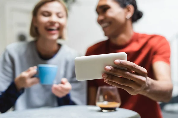 Smartphone en la mano del hombre afroamericano borroso cerca de la novia en la cafetería - foto de stock