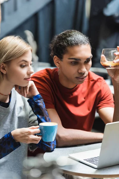 Young interracial freelancers holding coffee near laptop in cafe — Stock Photo