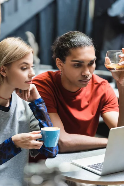 Joven interracial freelancers celebración de café cerca de la computadora portátil en la cafetería - foto de stock