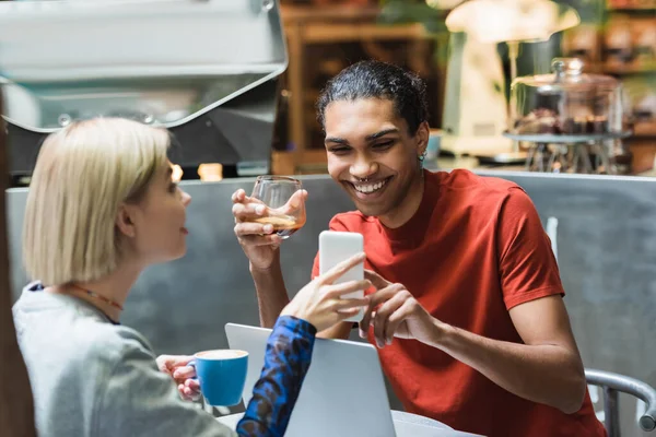 Cheerful multiethnic freelancers with coffee using devices in cafe — Stock Photo