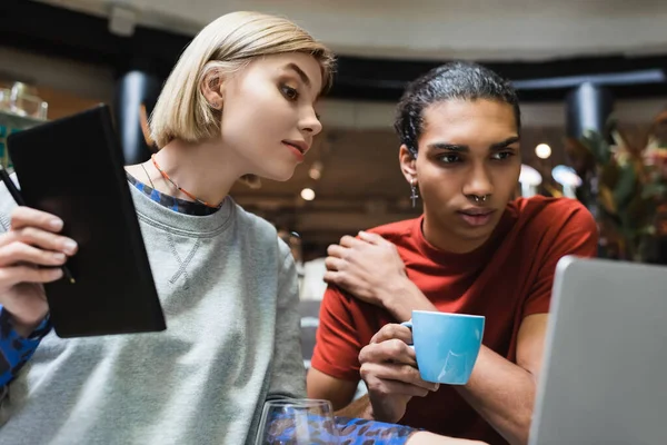 Multiethnic freelancers with laptop and notebook near laptop in cafe — Stock Photo