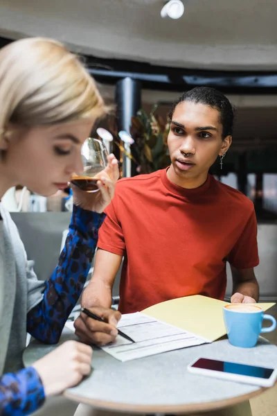 African american man holding paper folder near friend with coffee in cafe — Stock Photo
