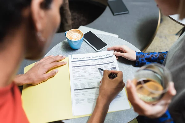 Multiethnic friends looking at papers in folder near cellphone and coffee in cafe — Stock Photo