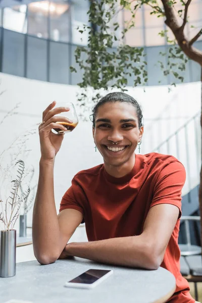 Sorridente uomo afro-americano che tiene il caffè vicino al cellulare nel caffè — Foto stock