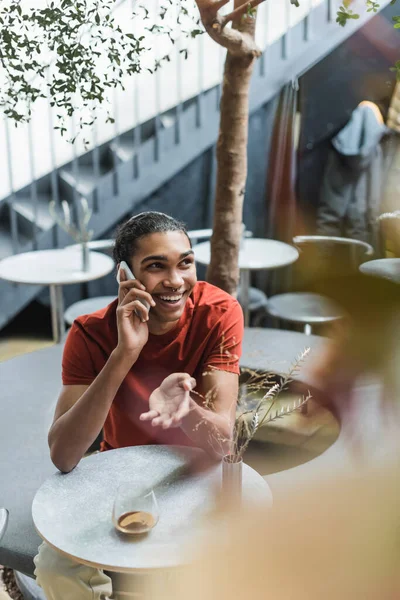 Позитивний афроамериканець розмовляє по мобільному біля кави у склянці в кафе. — стокове фото
