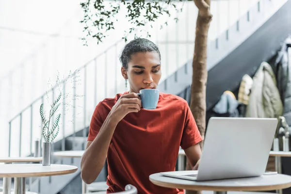 African american freelancer drinking coffee and using laptop in cafe — Stock Photo