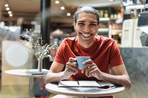 Joyeux homme afro-américain souriant à la caméra tout en tenant un café près d'un ordinateur portable dans un café — Photo de stock