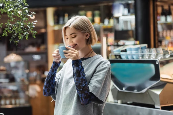 Позитивная женщина с закрытыми глазами держит чашку в кафе — стоковое фото