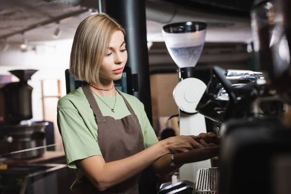 Блондинка-бариста в фартуке работает с кофемашиной в кафе — стоковое фото
