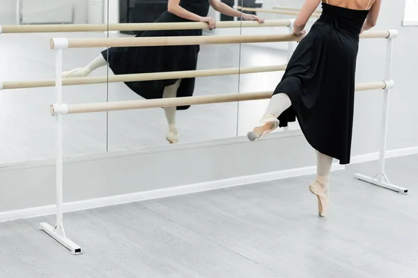 Cropped view of ballet dancer in black dress training at barre in studio — Stock Photo