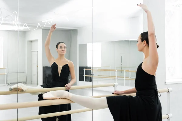 Brünette Ballerina schaut in den Spiegel, während sie im Tanzsaal an der Barre trainiert — Stockfoto