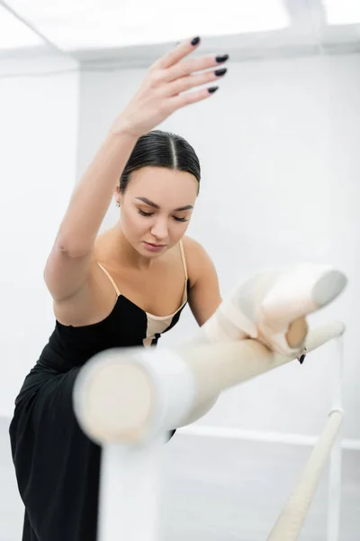 Jovem bailarina alongamento no barre em estúdio em primeiro plano borrado — Fotografia de Stock