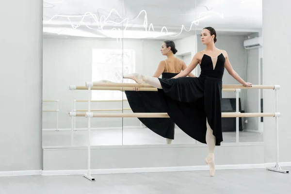 Vista completa de bailarina elegante practicando elementos de ballet cerca de espejos - foto de stock