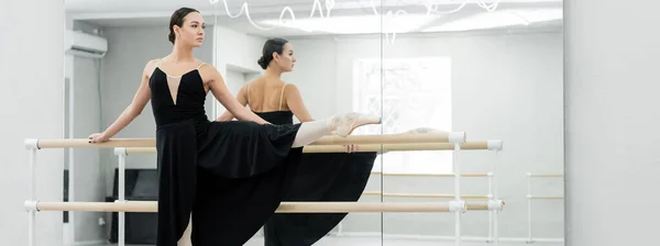 Joven bailarina en vestido negro ensayando cerca de espejos en el estudio, pancarta — Stock Photo