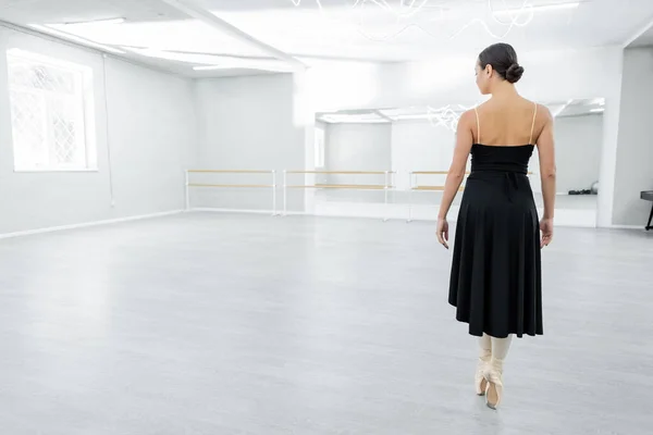 Visão traseira da bailarina em sapatos pontiagudos em pé sobre os dedos dos pés durante a repetição no salão de dança — Fotografia de Stock
