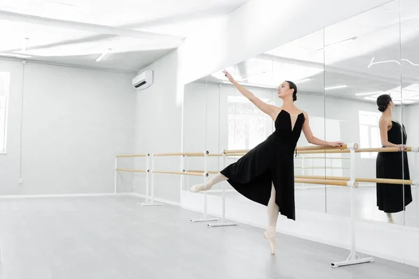 Graceful woman in black dress rehearsing near mirrors in ballet studio — Stock Photo