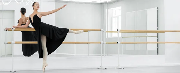 Slim and graceful ballerina practicing ballet elements at barre in studio, banner — Stock Photo