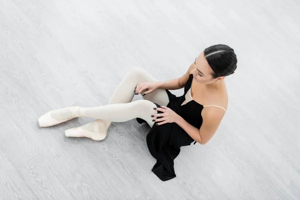 Vista aérea de la joven bailarina en vestido negro sentado en el suelo en el estudio - foto de stock