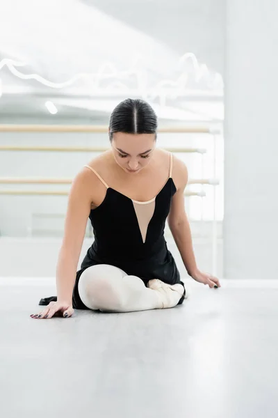 Young dancer in black dress stretching on floor in ballet studio — Stock Photo