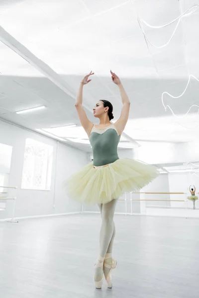 Young ballerina in tutu dancing with raised hands during rehearsal in studio — Stock Photo