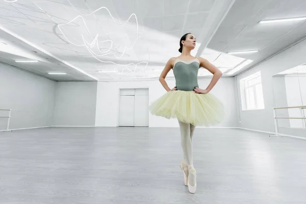 Full length view of woman in tutu dancing with hands on hips in ballet studio — Stock Photo