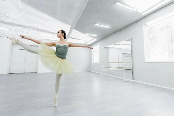 Ganzkörperansicht einer schlanken Frau im Tutu, die mit ausgestreckten Händen im Ballettstudio tanzt — Stockfoto