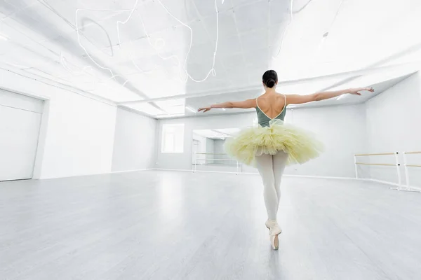 Back view of ballerina in tutu dancing with outstretched hands in studio — Stock Photo