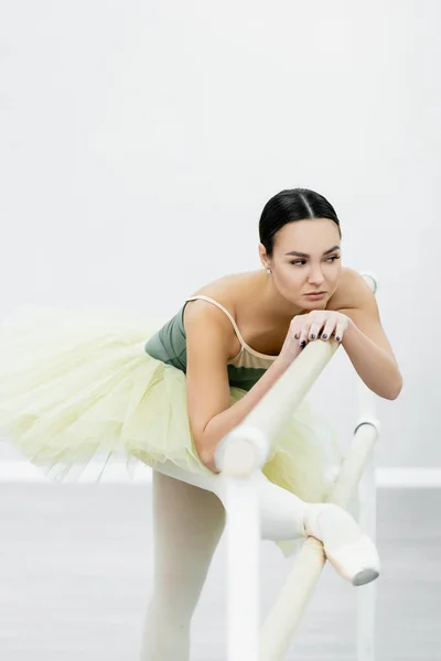 Ballerina in tutu stretching at barre while training in studio — Stock Photo