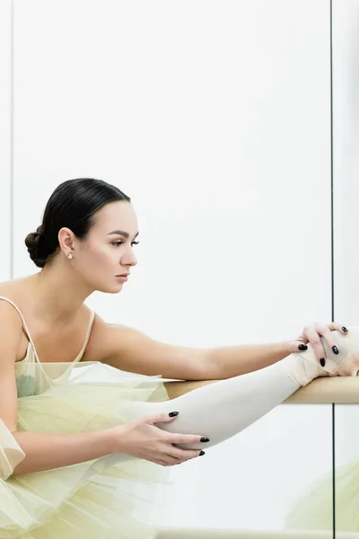 Young ballerina stretching leg at barre in dance studio — Stock Photo