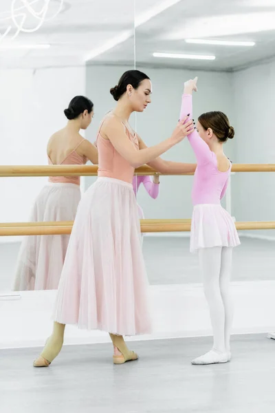 Vue pleine longueur du maître de ballet levant la main de la fille près de la barre et des miroirs en studio — Photo de stock