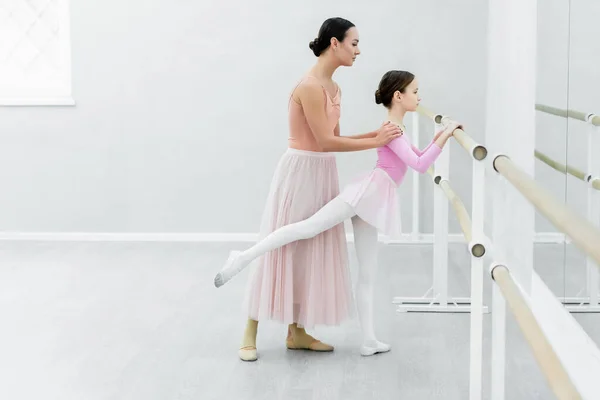 Vue latérale de l'enfant faisant de l'exercice à la barre près d'un professeur de ballet gracieux — Photo de stock