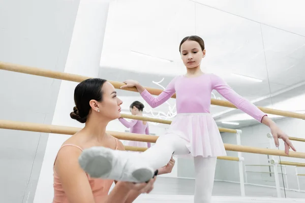 Молодий вчитель танців тримає ногу дівчини, що практикується в балетній школі — стокове фото
