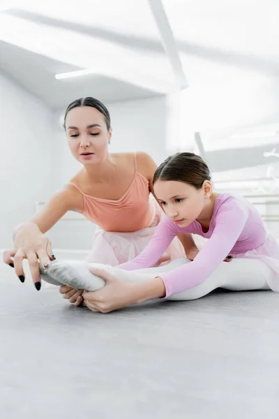 Coreógrafo ayudar chica estiramiento en piso en ballet escuela - foto de stock