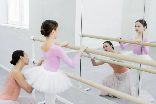 Niño mirando en el espejo mientras se entrena en la barra cerca de un joven profesor de ballet - foto de stock