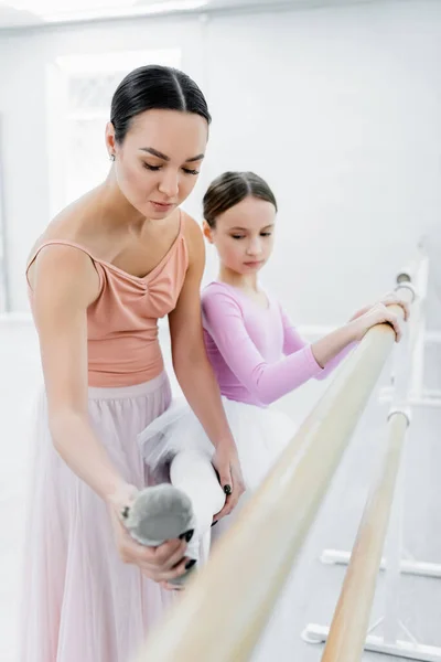 Young ballet teacher helping girl stretching during rehearsal in studio — Stock Photo