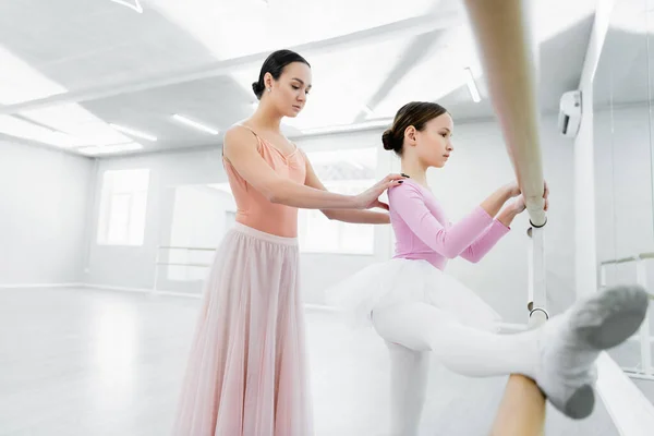 Chica delgada haciendo ejercicio en la barra cerca de elegante profesor de ballet en el estudio de baile - foto de stock