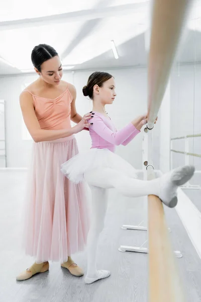 Preadolescente chica estiramiento en ballet escuela cerca joven coreógrafo - foto de stock