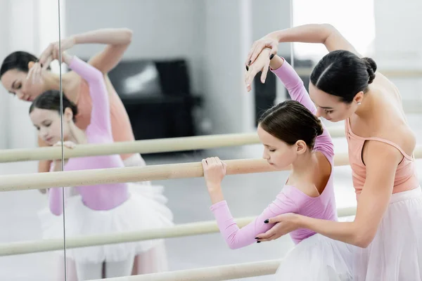Maestro de ballet ayudando a la niña preadolescente a entrenar en la barra cerca de espejos - foto de stock