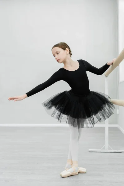 Visão de comprimento total da menina graciosa no treinamento de traje de balé preto no salão de dança — Fotografia de Stock