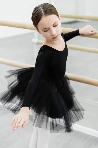Preteen girl in black ballet costume exercising at barre in studio — Stock Photo