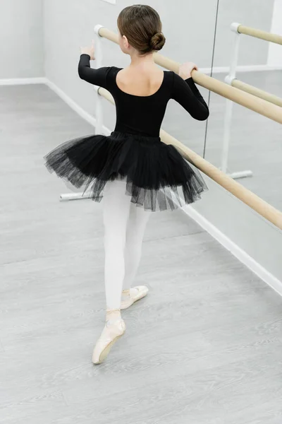 Vue arrière de l'enfant en costume de ballet noir pratiquant près de barre en studio — Photo de stock