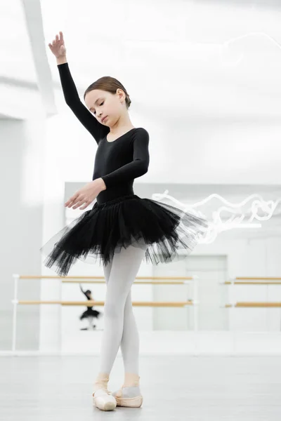 Sottile ragazza in nero tutu danza con alzato mano in studio di danza classica — Foto stock