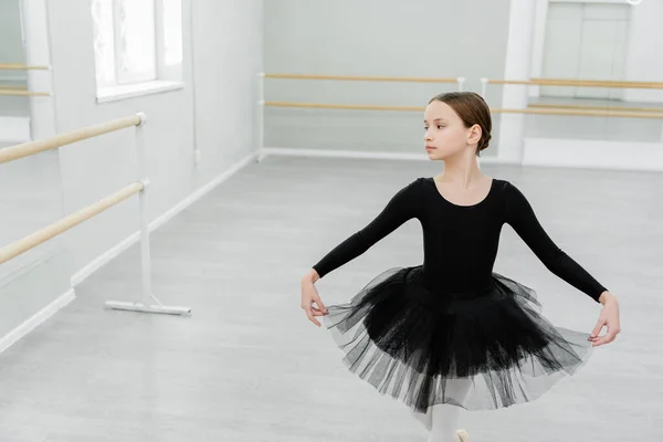 Ragazza in costume da balletto nero facendo curtsy mentre si allena nella sala da ballo — Foto stock